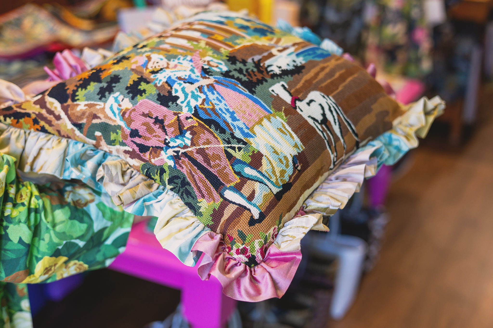 A decorative throw pillow with a colorful tapestry and ruffled edges in a shop setting.