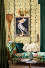 A cozy room with green floral wallpaper, a vintage chaise lounge with a green velvet pillow, oars, and a framed pelican print