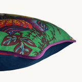 Sideshot of a square linen cushion with a bright emerald background and large scale bunch of interesting flowers and branches in yellow, red, navy and chocolate.