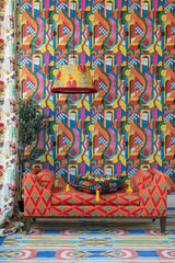 lounge nook with BOSSA NOVA wallpaper, a red patterned chaise, a tassel-adorned cushion, and a statement pendant lamp.