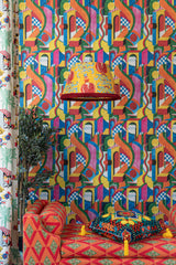 Bold, multicoloured geometric wallpaper -bossa nova - with abstract arches dominates the room, complemented by a patterned chaise, lamp, and cushion.