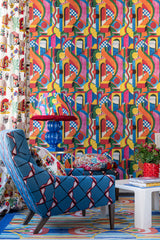 Bold geometric wallpaper with abstract arches, a blue patterned armchair, vibrant lamp, colourful cushions, and eclectic decor.
