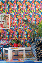 Room with vibrant BOSSA NOVA wallpaper, bold geometric patterns, a plush blue leopard print sofa, colourful accents, lush greenery, and eclectic decor.