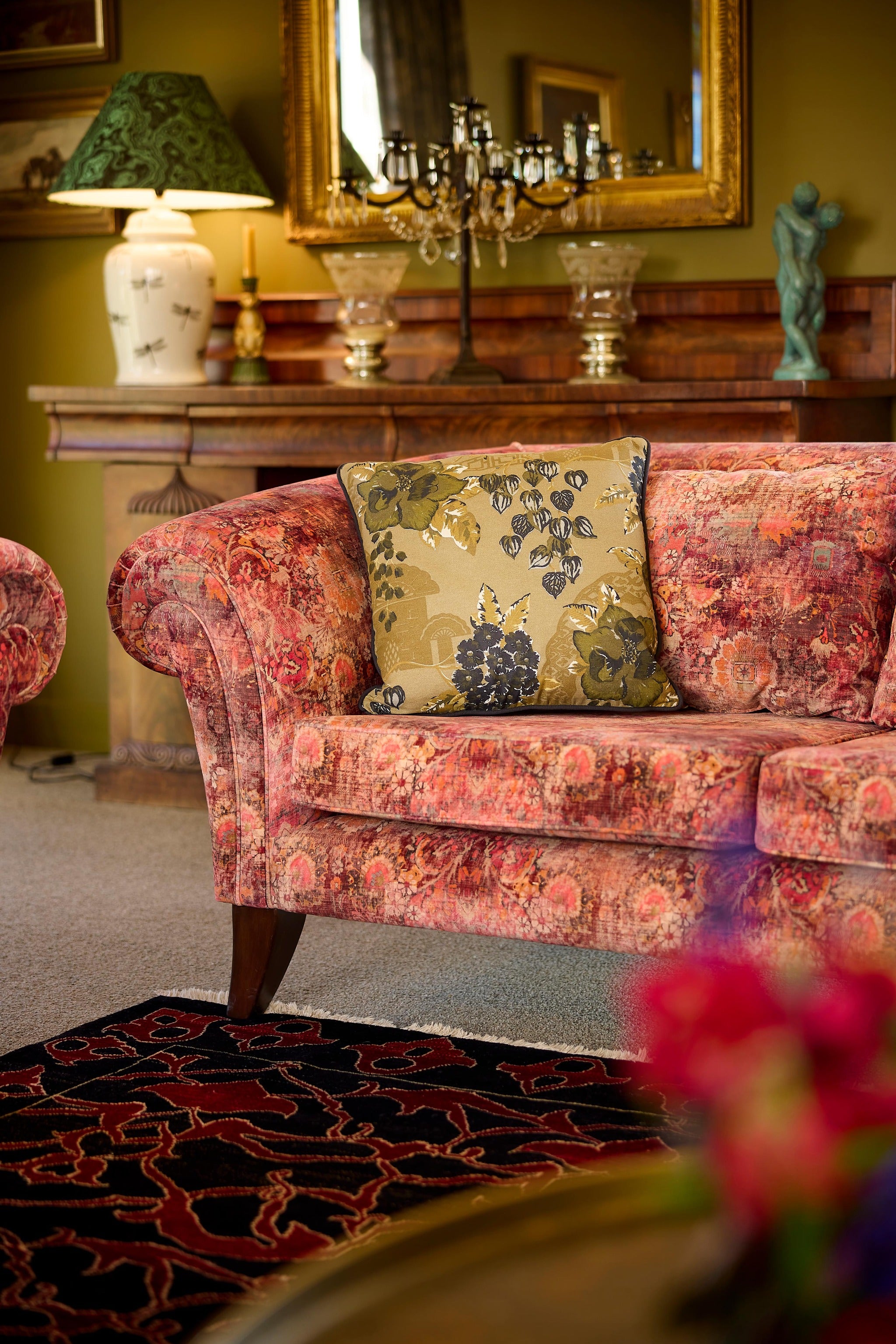 In situ photo of a khaki black and olive cushion on a red and orange velvet sofa.
