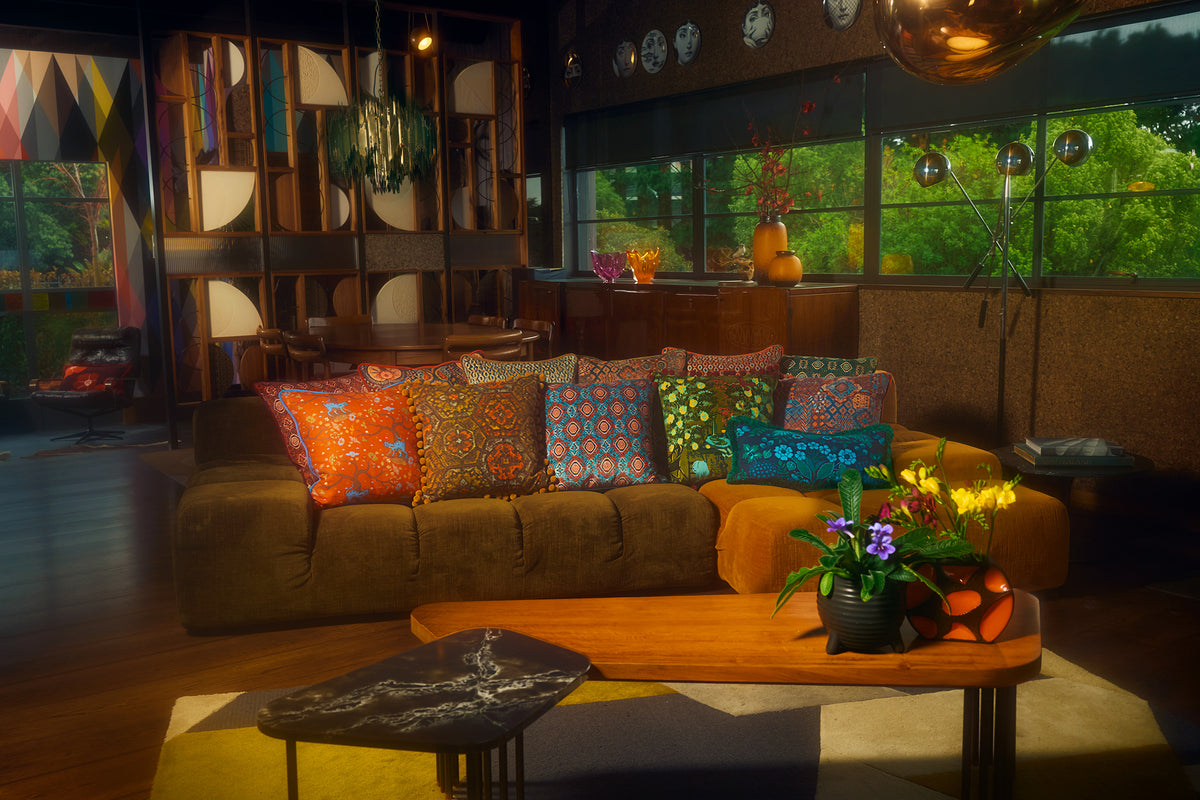 A cozy living room scene featuring a brown sectional sofa adorned with a variety of colorful patterned throw pillows, set in front of a wooden coffee table and a black marble side table.