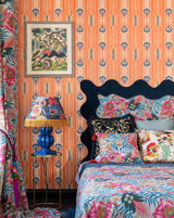 Vibrant bedroom with CARAMELLA Orangina wallpaper, floral bedding, bold blue headboard, and eclectic decor for a lively, maximalist aesthetic