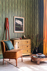 A lush green wallpaper with intricate reed-like foliage adds depth to a cozy space with a rustic wooden dresser and vintage decor