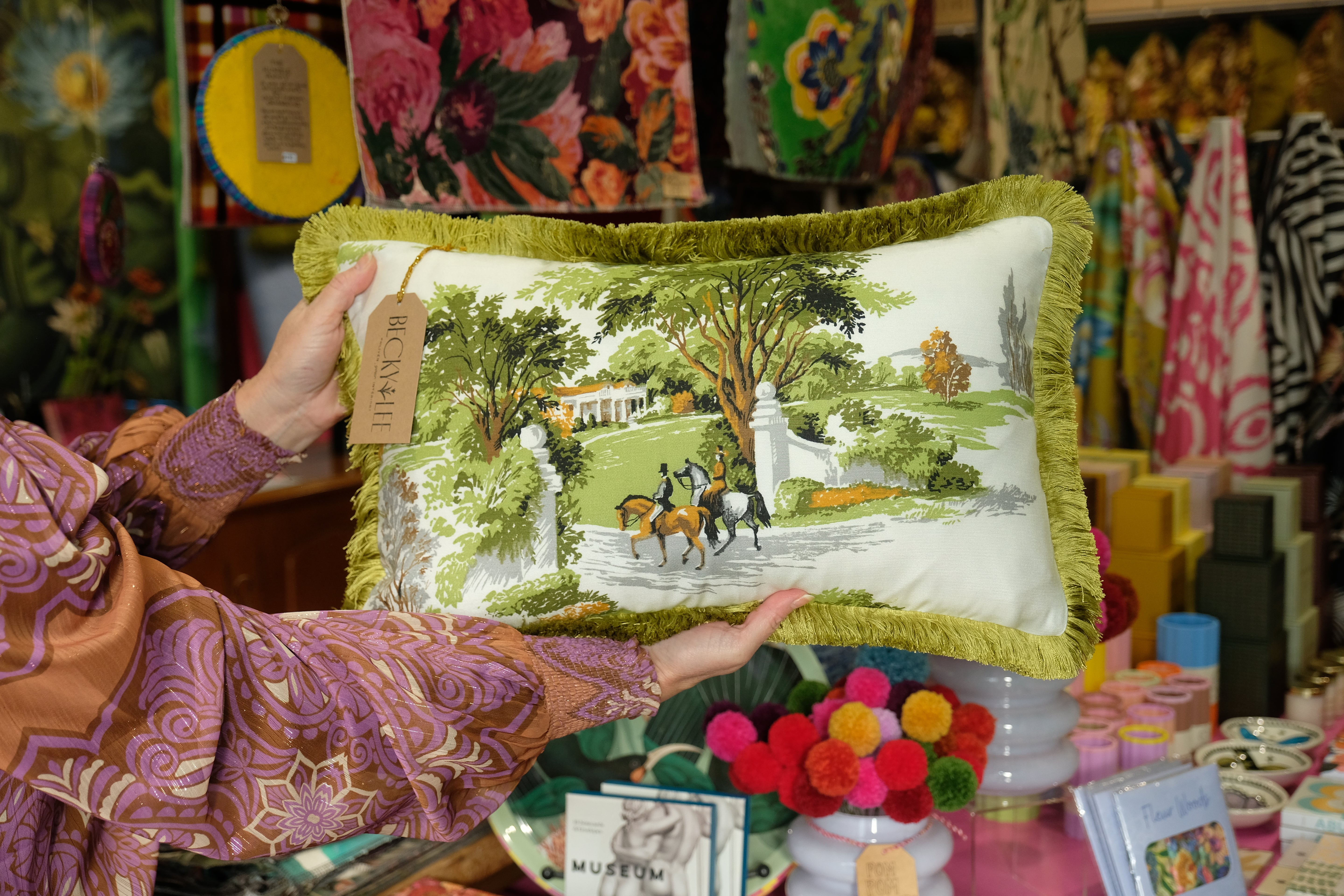 Person holding a decorative pillow with a scenic design in a store setting