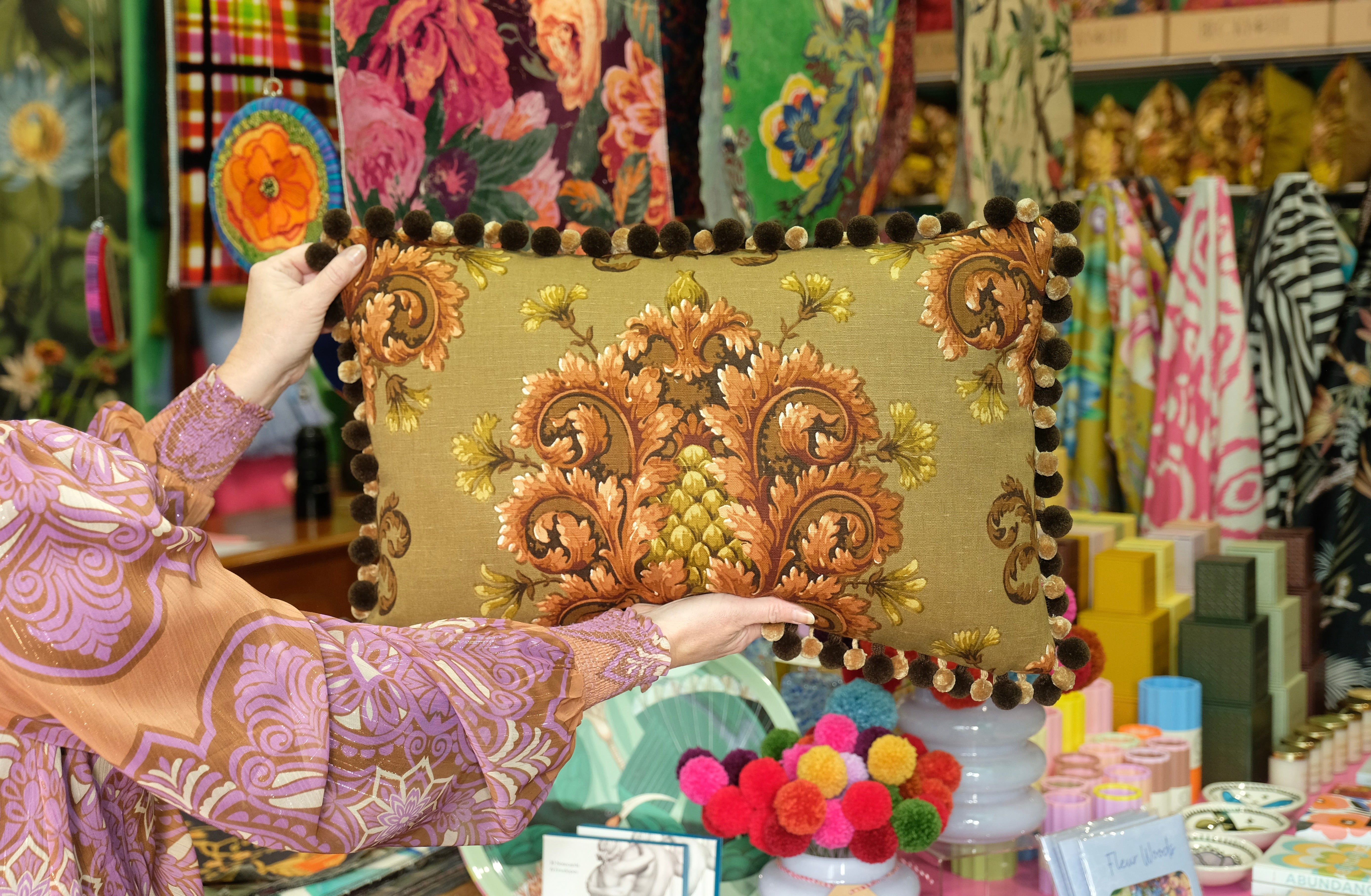 Person holding a decorative cushion with intricate designs in a colourful cushion boutique