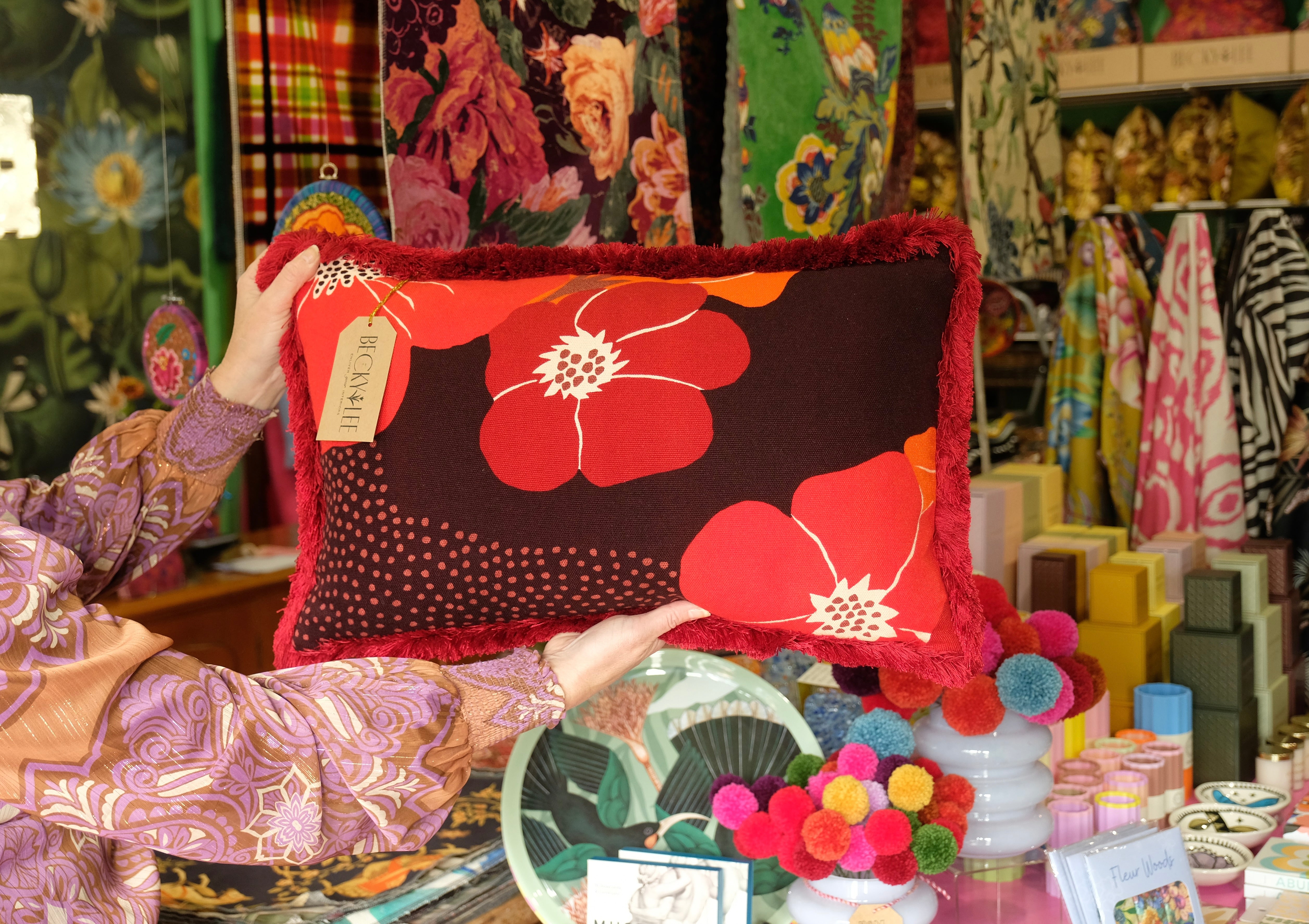 Person holding a red floral pillow in a colorful fabric store