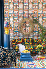 Luxe living space with ornate architectural EL CIRCO wallpaper, a bold patterned sofa, a blue leopard-print chair, and a striking gold sunburst mirror.