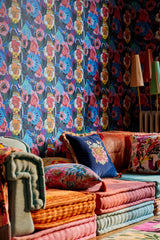 Cozy lounge with bold FIORI IN FIORE floral wallpaper, layered cushion seating, embroidered pillows, and vintage-inspired floor lamps in warm, rich tones.