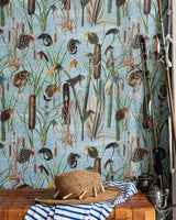 A fishing-themed wallpaper featuring reeds, cattails, and colourful fishing flies sets a rustic backdrop for a straw hat, striped towel, and fishing rods