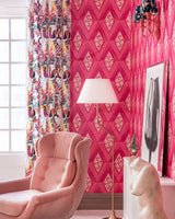 A statement pink geometric wallpaper with diamond motifs enhances a cozy interior with a blush armchair, gold lamp, and artistic decor