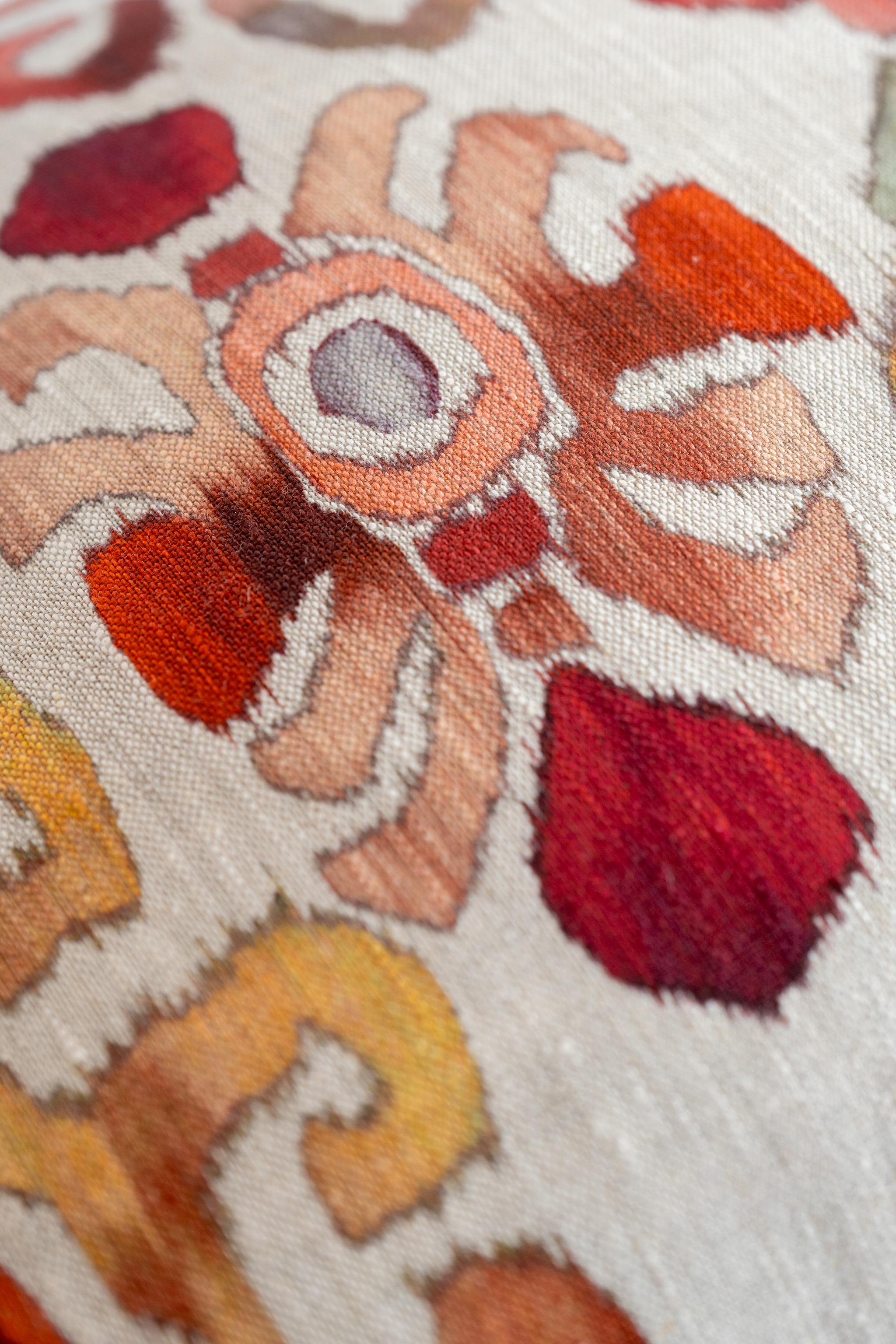 Close-up of a textured linen with intricate patterns in red, orange, and beige.