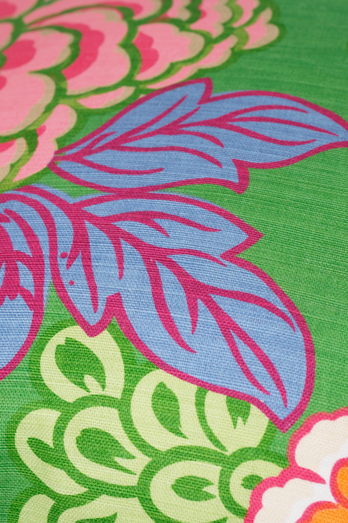 A close-up of a colorful floral patterned fabric, featuring light blue leaves with magenta outlines on a bright green background, with pink and yellow flowers at the edges.