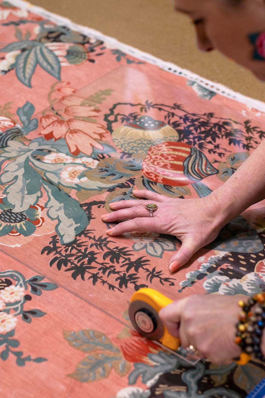 Person cutting fabric with floral patterns using a rotary cutter.