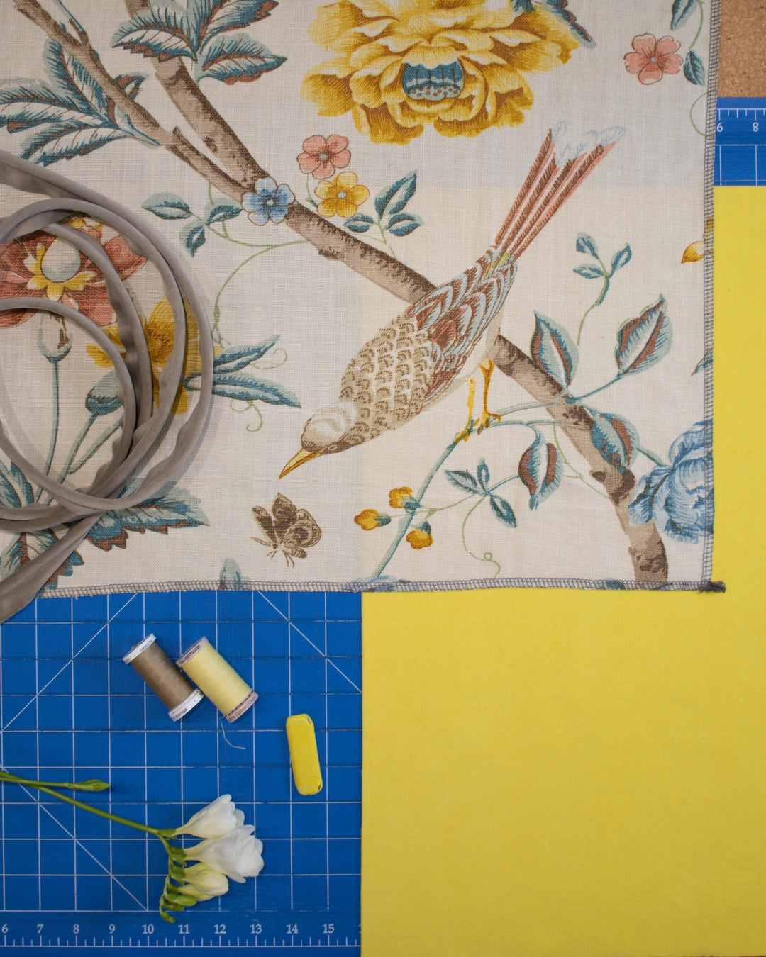 Fabric with bird and floral pattern on a cutting mat with sewing materials.