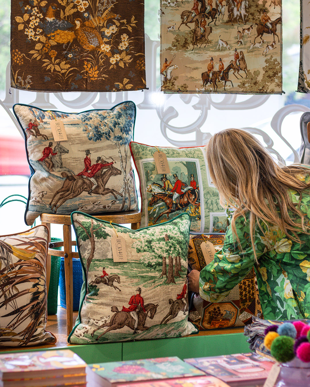 Woman looking at decorative pillows with hunting scene designs in a store.