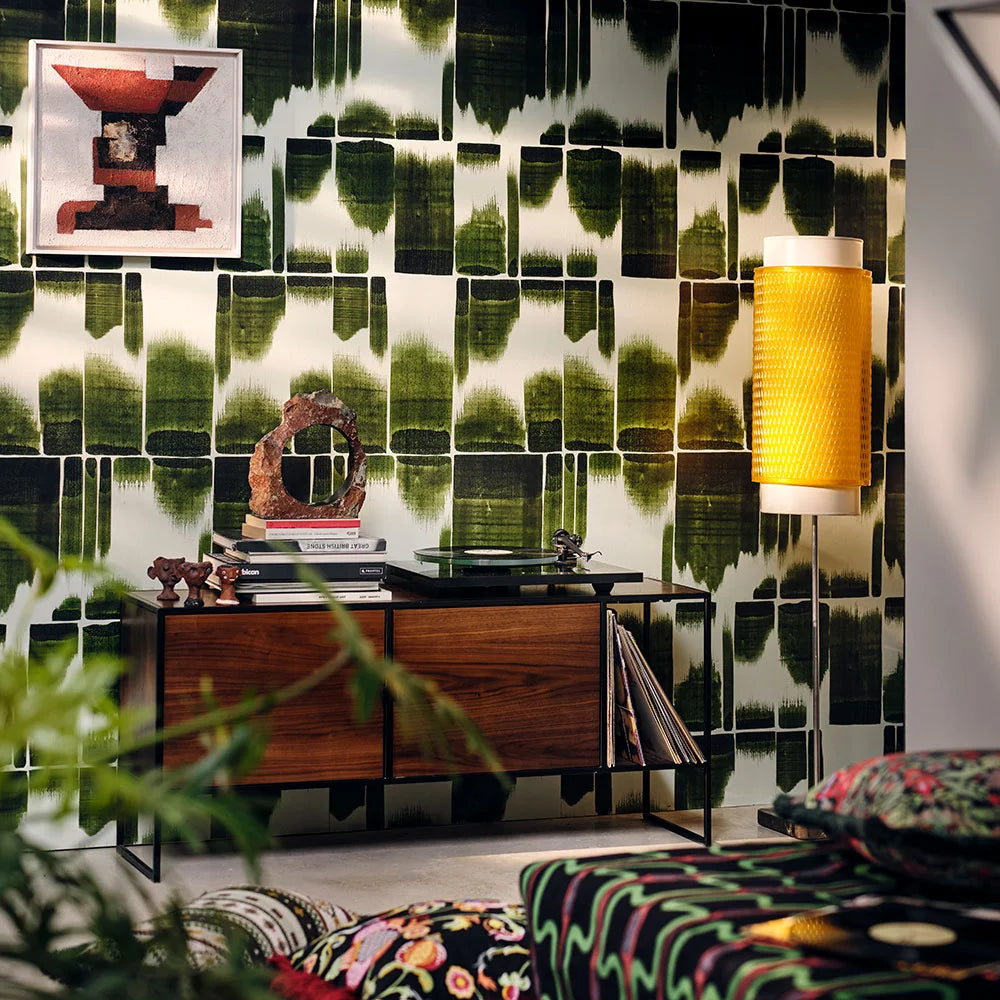 Green abstract brushstroke wallpaper with a mid-century console, books, sculpture, and a yellow textured wall light in a cozy living room.