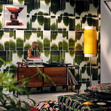 Green abstract brushstroke wallpaper with a mid-century console, books, sculpture, and a yellow textured wall light in a cozy living room.