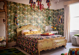 Vintage-inspired bedroom with floral café-scene wallpaper LA BRASSERIA Fern - an ornate bed, bold patterned bedding, a marble sink, and a colourful chandelier.