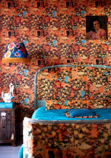 Bedroom with LA BRASSERIA Salmon wallpaper featuring vintage café scenes, a matching upholstered bed, blue bedding, a fringed lamp, and antique decor