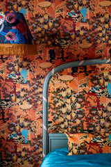 Bedroom with LA BRASSERIA Salmon wallpaper featuring vintage café scenes, a matching upholstered headboard, a blue bedspread, and a fringed lamp.