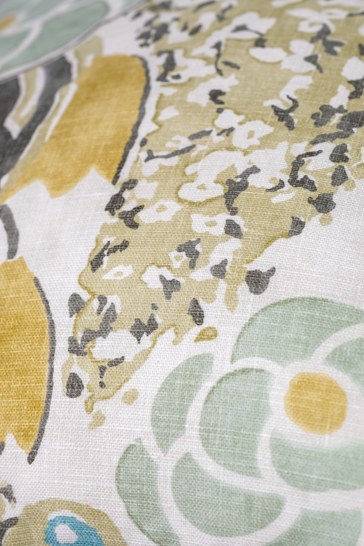 A close-up of a woven fabric with a retro floral pattern in sage green, mustard yellow, and dark gray on a white background.