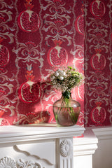 Close-up of MELAGRANATA wallpaper with intricate pomegranate motifs, a white ornate mantel, and a glass vase filled with delicate flowers.