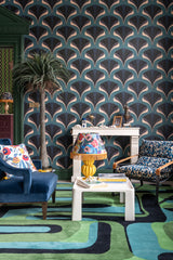 Sophisticated living space with MEZZELUNE Kale wallpaper, a bold geometric rug, velvet armchairs, a fringed lamp, and an ornate fireplace.