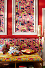 Vibrant room featuring MOTO BELLO Pink wallpaper, bold red walls, a patterned daybed with colourful cushions, and elegant floor lamps.