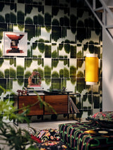 Green graphic wallpaper with black pattern behind a mid-century sideboard, art print, yellow wall lamp, and vinyl records in a cozy music room.