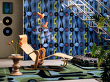 Living space featuring bold blue wallpaper with geometric black, red, and green motifs, styled with a sculptural wooden chai