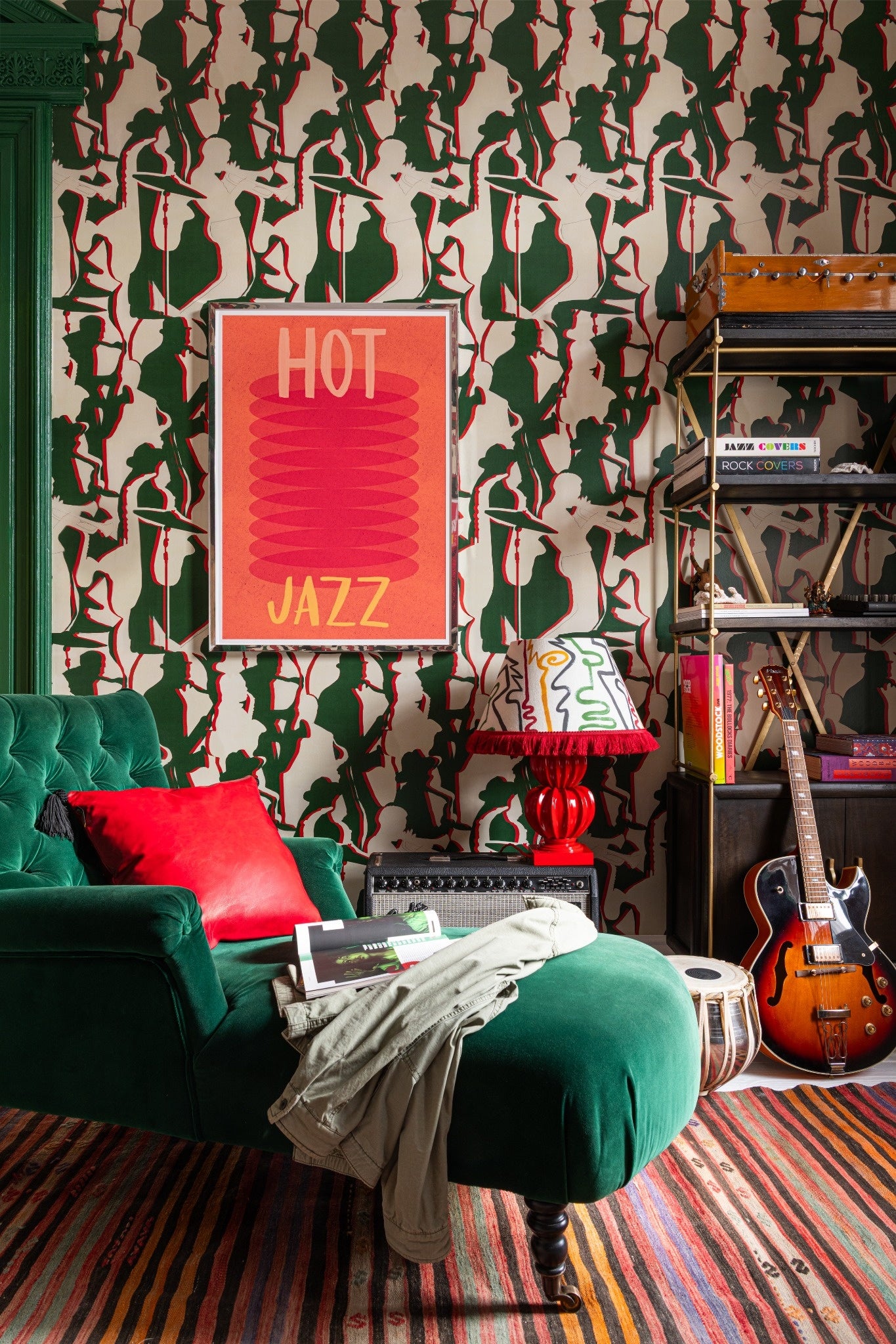 Mind The Gap Tripping Green wallpaper with flowing organic forms behind cozy lounge furniture, a striped rug and guitar resting in front of shelving