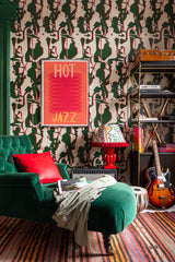 Mind The Gap Tripping Green wallpaper with flowing organic forms behind cozy lounge furniture, a striped rug and guitar resting in front of shelving