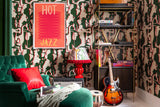 Eclectic seating area featuring Mind The Gap Tripping Green abstract organic patterned wallpaper, a framed poster, electric guitar and shelving holding books
