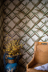 A close-up of botanical lattice wallpaper with interwoven reeds, a blue decorative vase with yellow flowers, and a wicker chair