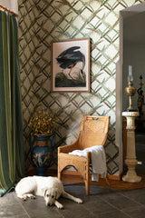 A serene space featuring green botanical lattice wallpaper, a wicker chair, vintage decor, and a resting white dog