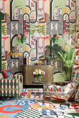 Bold and eclectic living space featuring PIACERI MONDANI wallpaper, geometric furniture, vibrant textiles, and lush greenery.