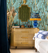 A luxurious bedroom with aquatic-inspired wallpaper, a gold dresser, and bold blue and gold decor. A plush white couch and natural light add elegance.