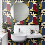 Modern bathroom with bold geometric wallpaper in red, green, blue, yellow, and black, featuring a round mirror above a white sink