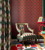 A bold red and green Art Deco-inspired wallpaper pairs with a geometric-patterned chair, a colourful lamp, and a vintage-style setting.