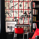 A music-themed study with red and cream wallpaper featuring black line art of instruments, a red chair, black piano, and framed jazz festival poster.