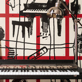 Close-up of wallpaper with black sketch-style musical instruments and red grid pattern behind a keyboard and silver lamp.