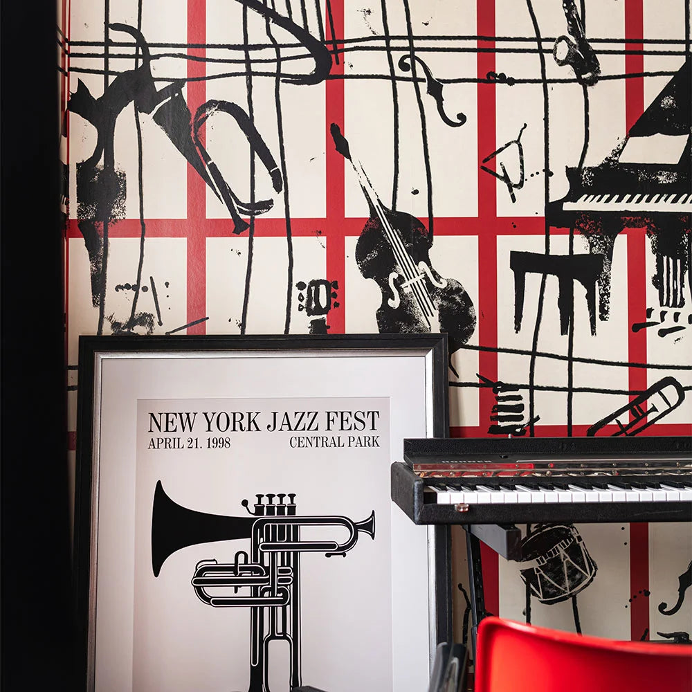 Room with red grid and black instrument wallpaper, a framed jazz fest poster, keyboard, and red chair.