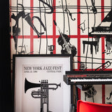 Room with red grid and black instrument wallpaper, a framed jazz fest poster, keyboard, and red chair.