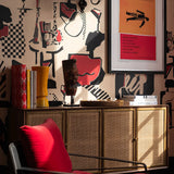 Close-up of abstract red and black jazz-themed wallpaper with decorative objects on a sideboard under framed artwork.