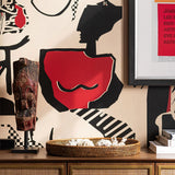 Detail of abstract red, black, cream wallpaper with silhouette shapes and geometric motifs behind sculpture and tray.
