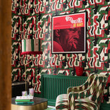 A living room with green, red and black abstract face print wallpaper, a red-fringed lamp, green radiator and a framed red Art Blakey poster.